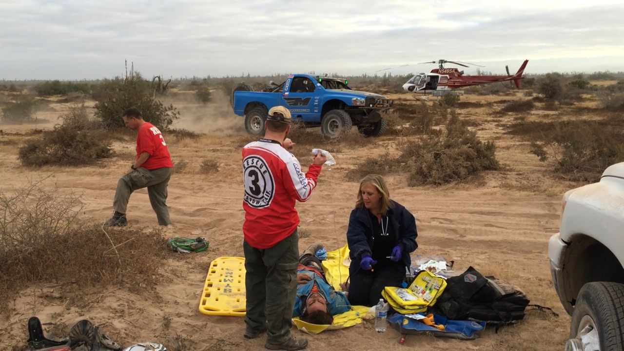Symbiosis medic treating a patient in the desert during the Baja 1000 with a race truck in the background